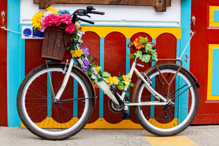 Bicycle covered in flowers leaning against a red, yellow and turquoise colored wall 