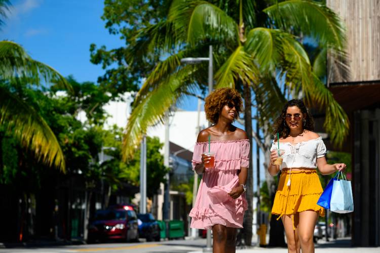 two women walking outside in tropical setting on sunny day with shopping bag