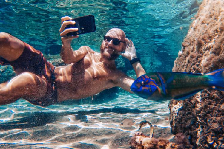 man taking a selfie posing with a fish underwater 